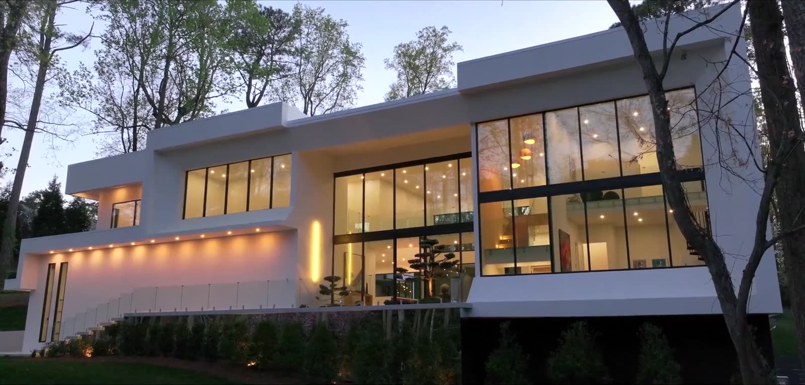 A contemporary luxury home at twilight, glass walls lit from within